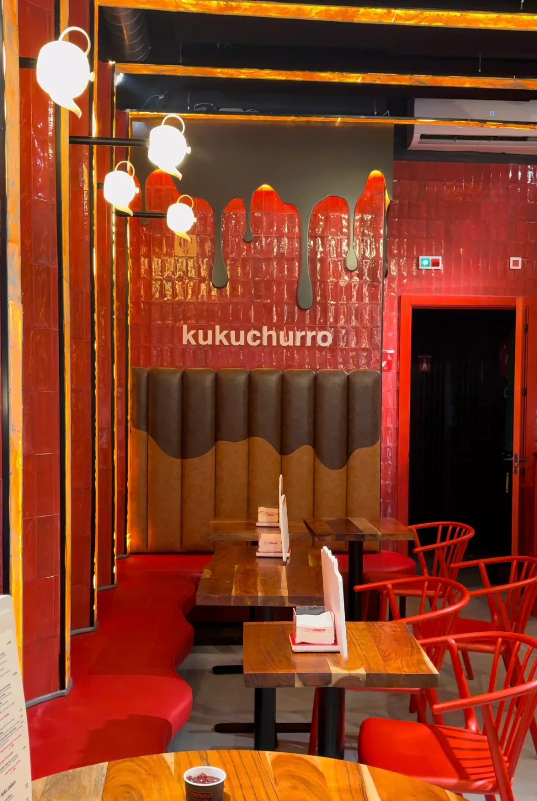 Inside Kukuchurro Regina, wooden tables, red chairs and the chocolate wall